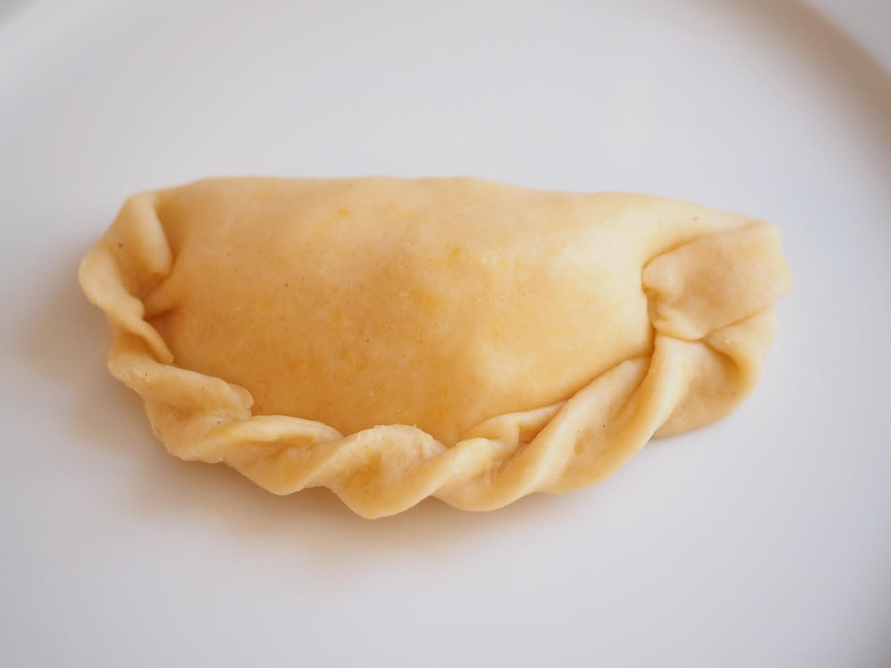 Casunzones dorati e croccanti disposti su piatto bianco, ripiena di patate gialle visibili al taglio, cosparsi di zucchero semolato, contorno di sugo rosso di pomodoro in ciotola