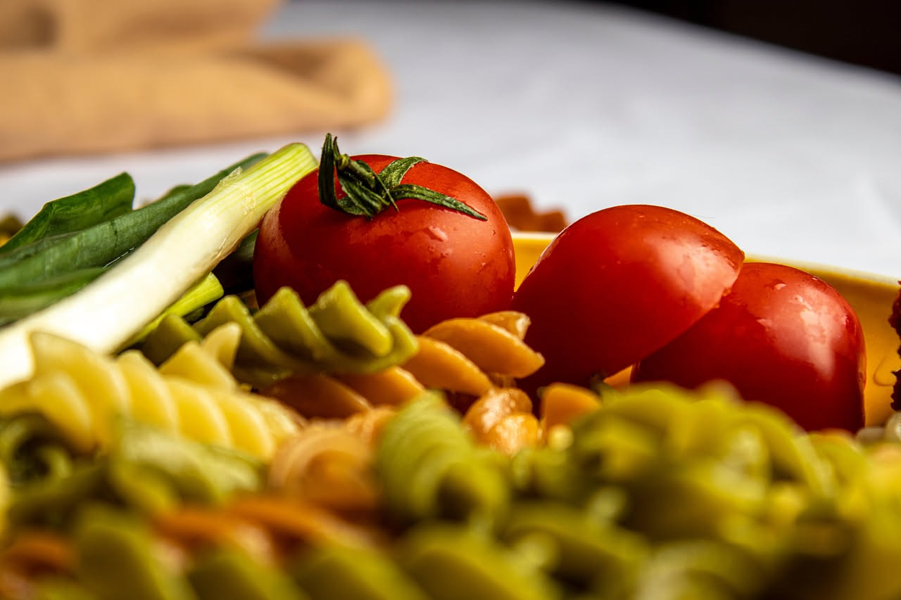 Piatto di cavatelli con sugo di pomodoro rosso vivo, olio verde oliva, basilico fresco sopra, serviti in piatto bianco ceramica con bordo leggero sfondo neutro