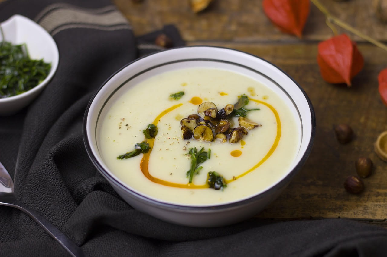 Cavolfiore bianco cotto in padella, pezzi morbidi e uniformi immersi in brodo chiaro con gocce d'olio dorato, aglio e prezzemolo tritato fresco in superficie