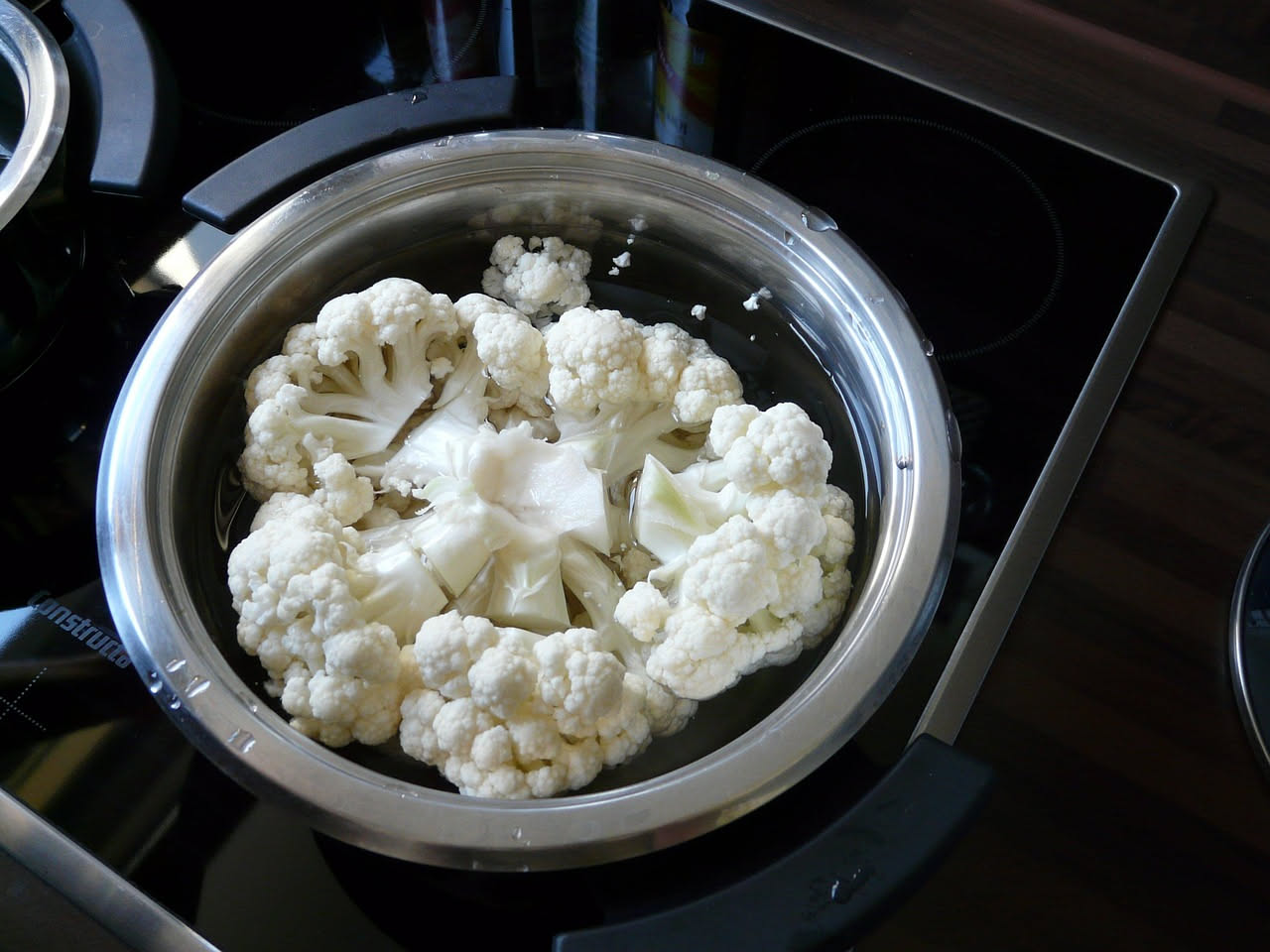 Vasetto di vetro con cavolfiore bianco tagliato sott'aceto, con alcuni grani di pepe nero e foglie di alloro visibili nel liquido trasparente