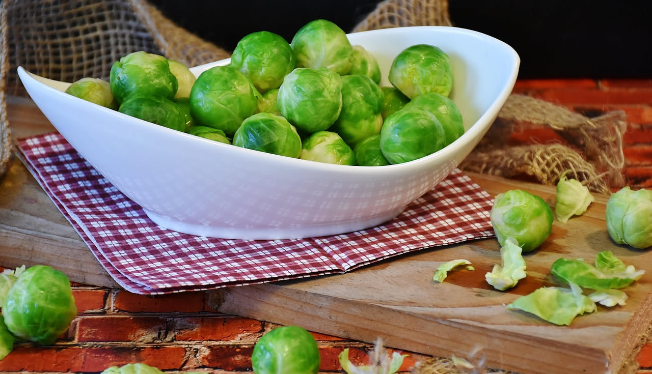 Cavolini di Bruxelles saltati in una padella antiaderente, dorati e croccanti, con superficie caramellata marrone scuro, spargimenti di aglio dorato e gocce d'olio lucido, ciotola bianca in primo pian
