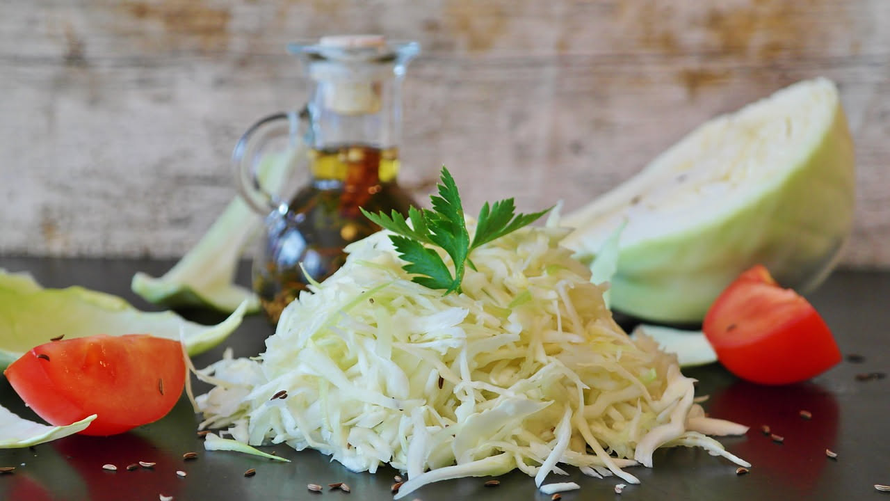 Cavolo cappuccio bianco a fette sottili, giallo oro dal condimento, in barattolo di vetro con olio trasparente e aglio visibile, foglie croccanti ben compatte