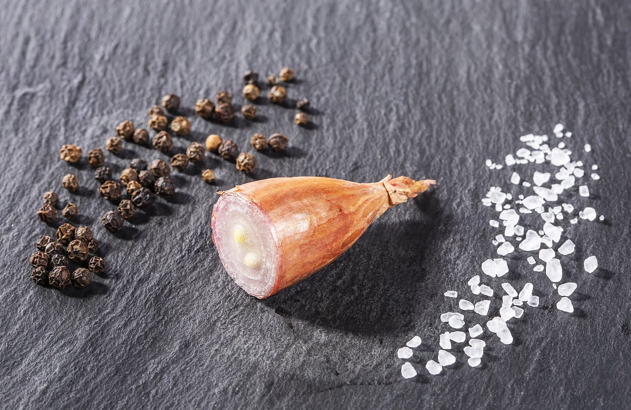 Fette sottili di cipolla friulana bianca e cruda, disposte a raggiera in un piatto bianco, cosparse di olio d'oliva verde e sale marino grosso, con qualche foglia di prezzemolo fresco