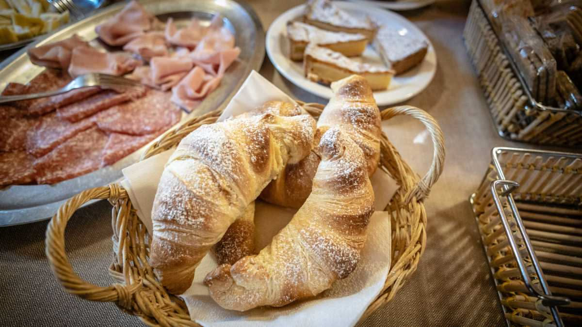 Coccoli toscani dorati e polverosi di zucchero, tagliati a metà per mostrare il ripieno di marmellata di albicocca, su un piatto bianco rustico