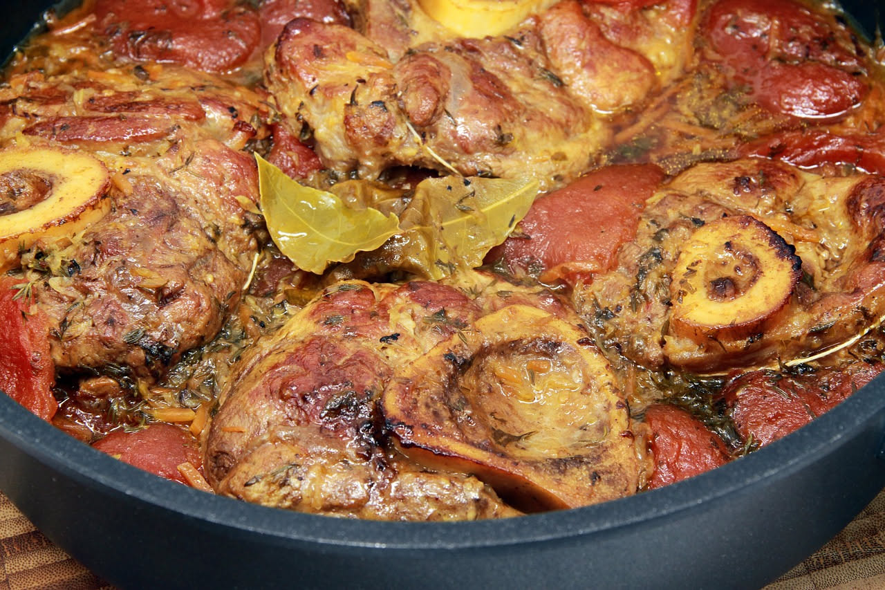 Coda di manzo brasata in pentola di coccio con pomodori rossi, sedano e brodo marrone scuro, pezzi di carne tenera visibili a fette spesse