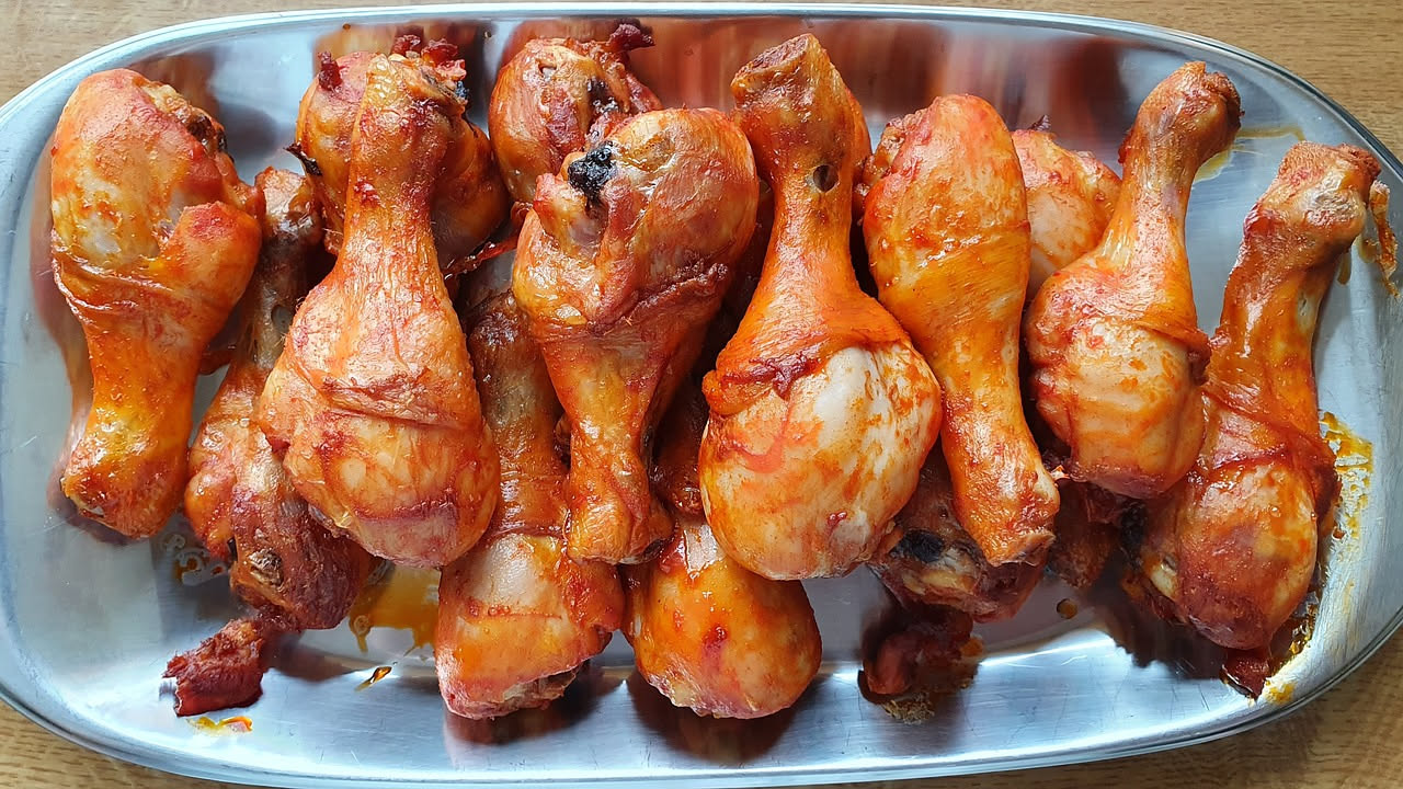 Cosce di pollo arrosto dorate e croccanti in una teglia rettangolare di ceramica, circondati da spicchi di limone, rosmarino fresco e patate tagliate a cubetti, su un piano di marmo chiaro