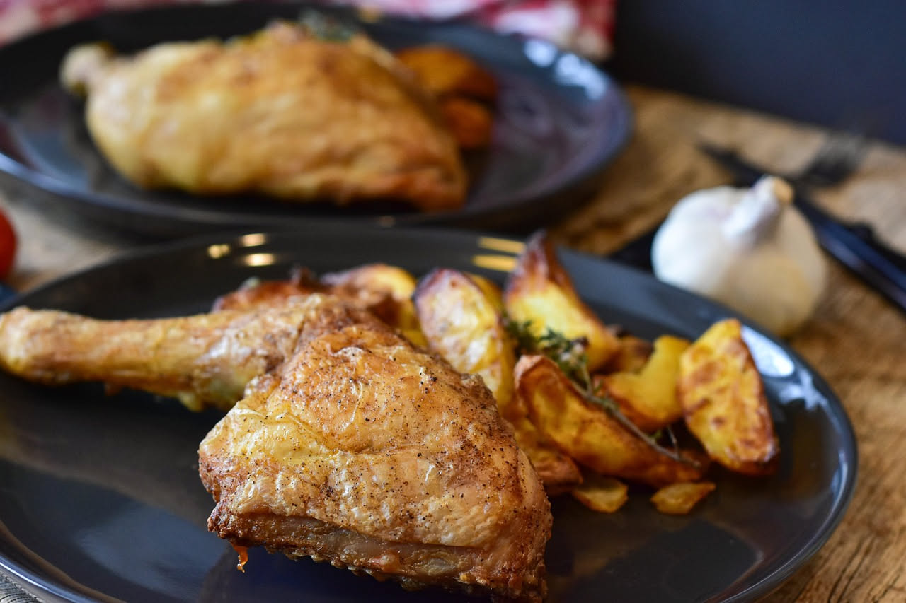 Cosce di pollo dorate e croccanti in una teglia da forno, ricoperte di buccia marrone brillante, accompagnate da patate e rosmarino fresco