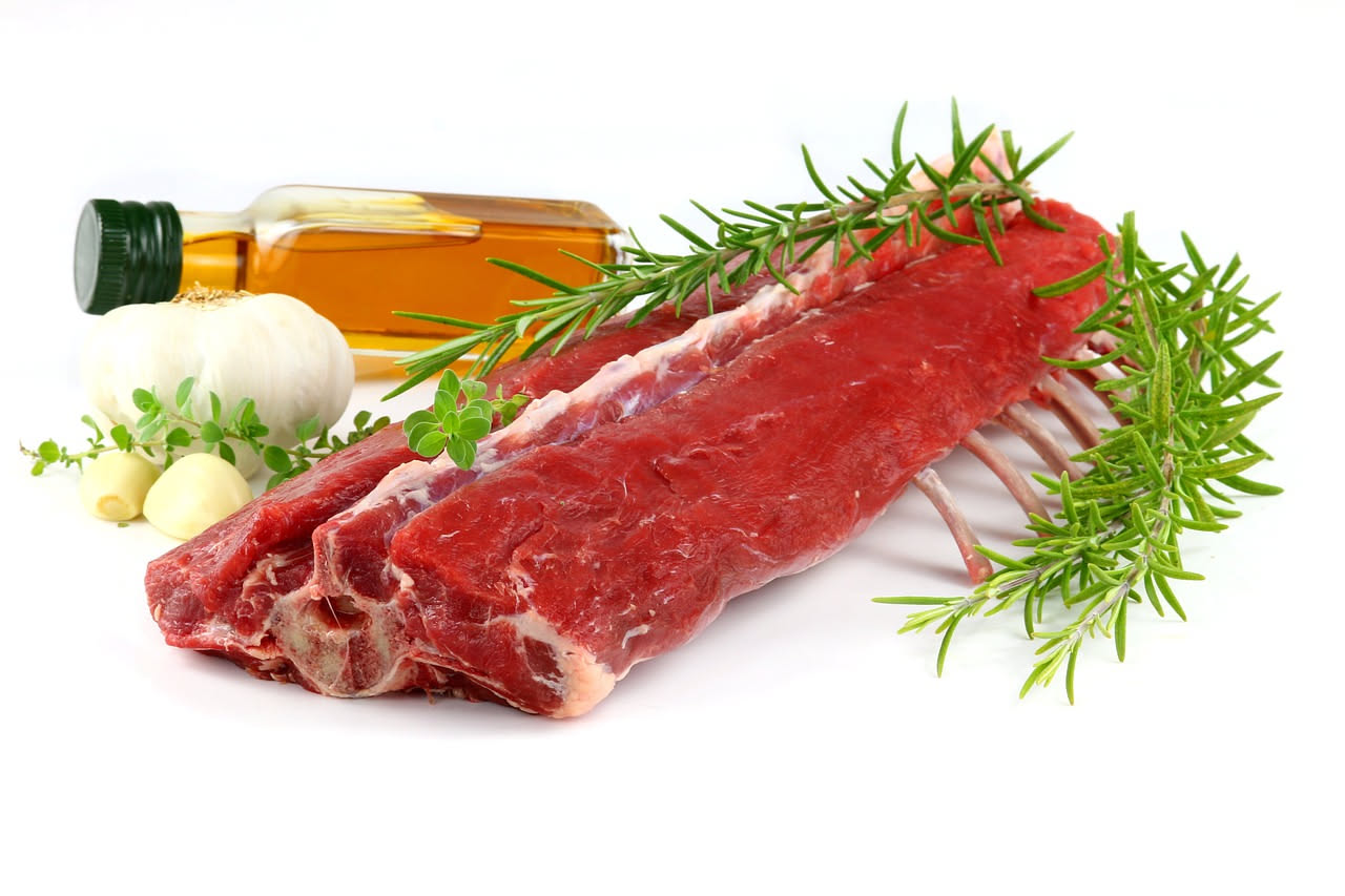 Tre costolette di capretto dorate con crosta rossiccia in una padella nera, contornate da rosmarino fresco e spicchi di limone, vapore che sale dalla superficie