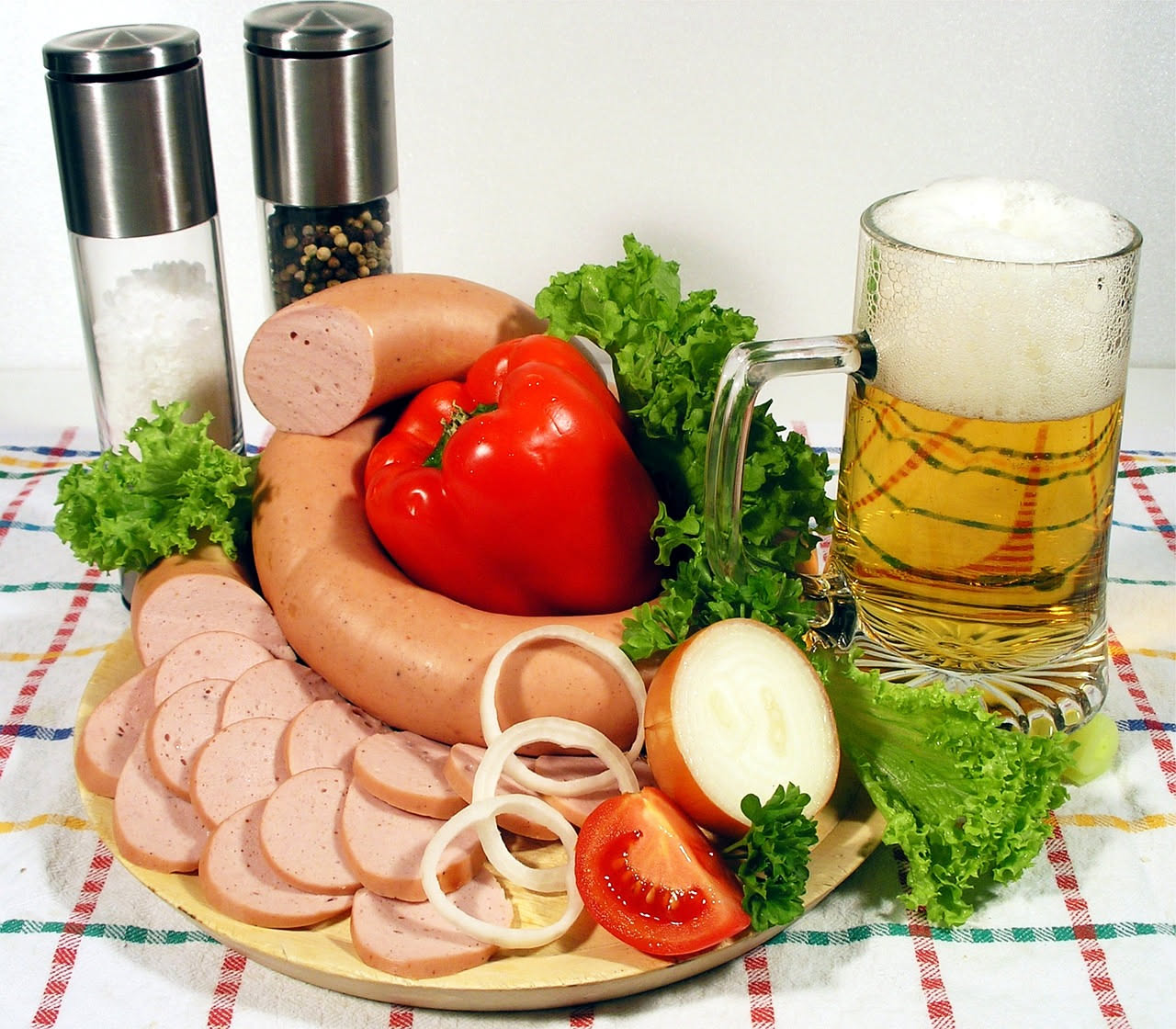 Cotechino affumicato intero tagliato a fette in un piatto bianco con brodo caldo, contorno di lenticchie rosse e cipolla cruda grattugiata accanto