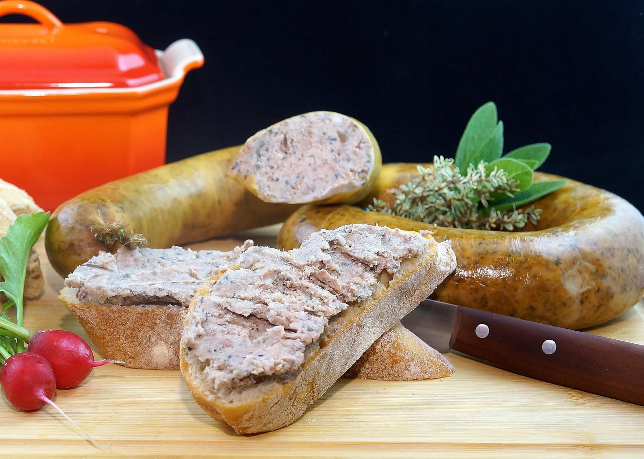 Cotechino intero in pentola con acqua calda, accanto fette dorate in padella di ferro con cipolla e erbe aromatiche