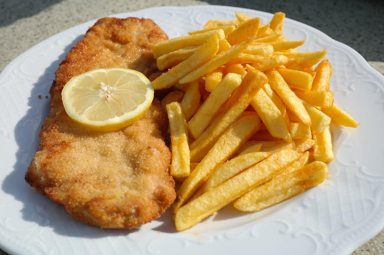Due cotolette alla milanese dorate e croccanti appoggiate su carta assorbente, con limone affettato e un contorno di verdure crude a lato, piatto bianco