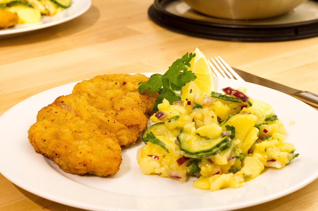 Due cotolette di vitella dorate e croccanti disposte su un piatto bianco con limone fresco affettato e prezzemolo verde, fondo sfumato in grigio chiaro