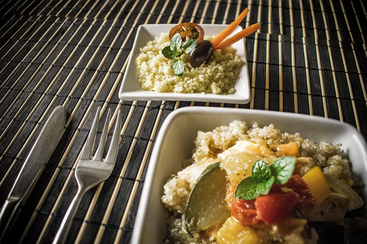 Piatto di couscous biondo dorato con gamberi rossi, pezzi di pesce bianco, cozze aperte e verdure colorate sparse in superficie, condito con olio e limone, servito su un piatto bianco con contorno di