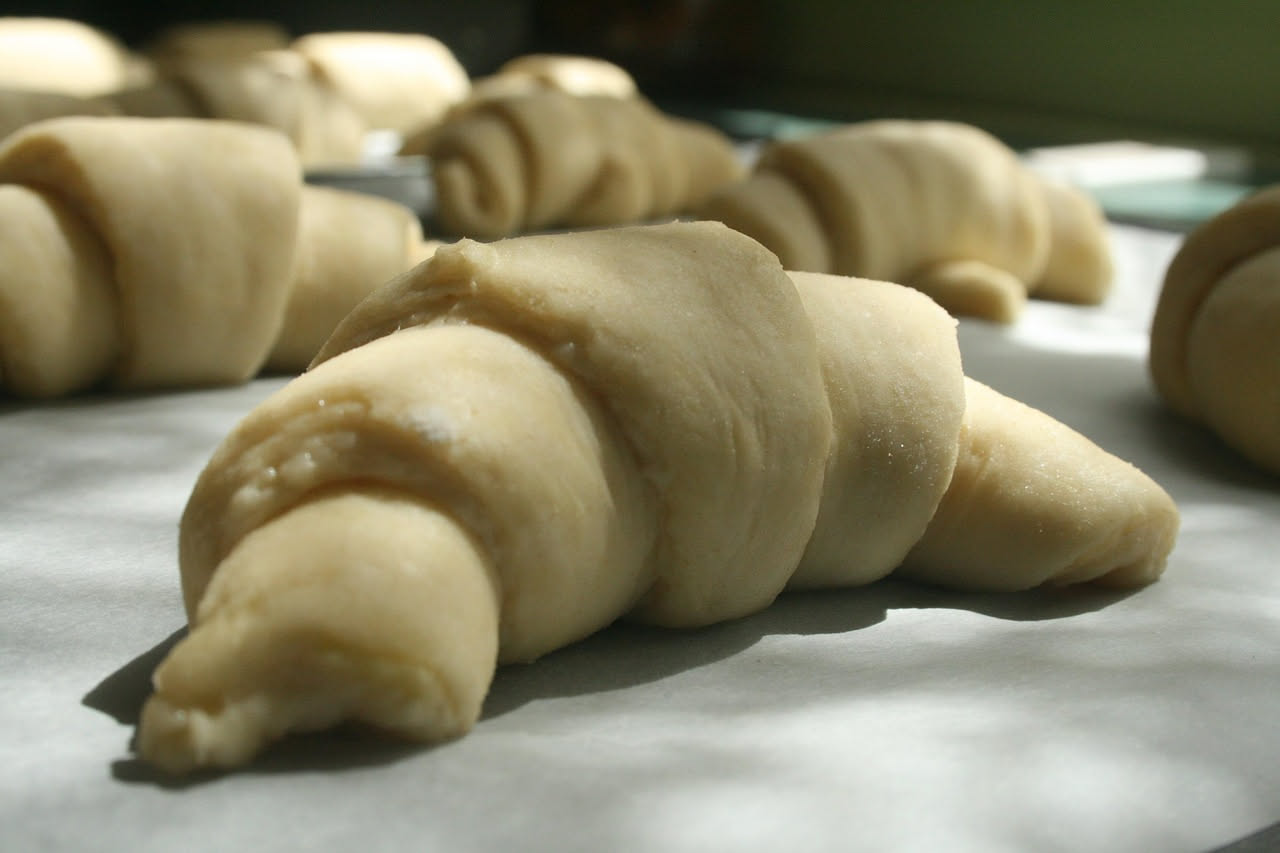 Crescente di pasta sfoglia dorata e croccante su piatto bianco, spezzato a metà per mostrare il ripieno cremoso, con briciole di sfoglia intorno e superficie caramellata