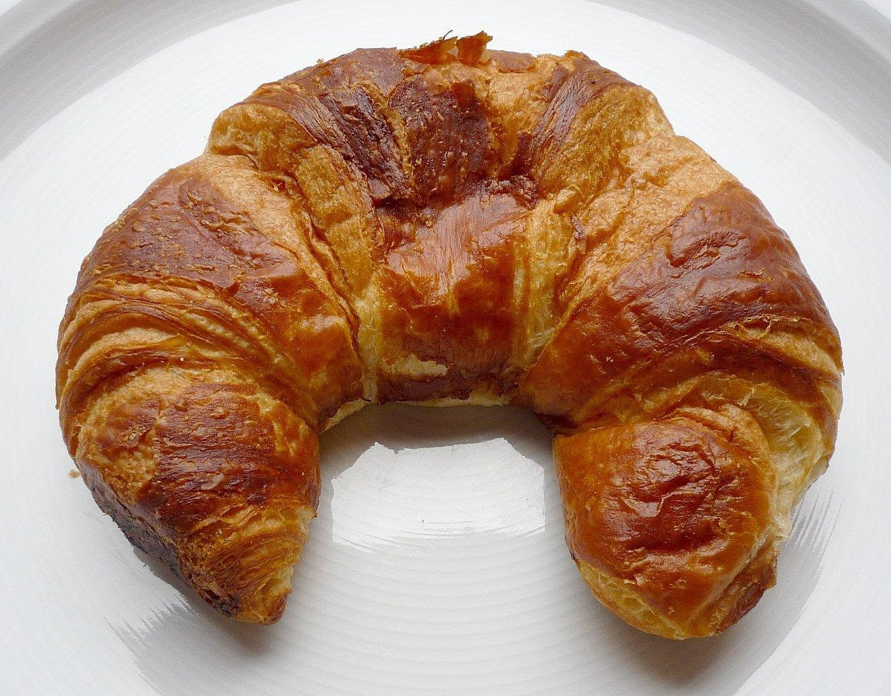 Crescente ripiena tagliata a metà, mostra l'interno dorato con prosciutto cotto e formaggio fuso, superficie superiore dorata e lucida, servita su piatto bianco con ingredienti sullo sfondo