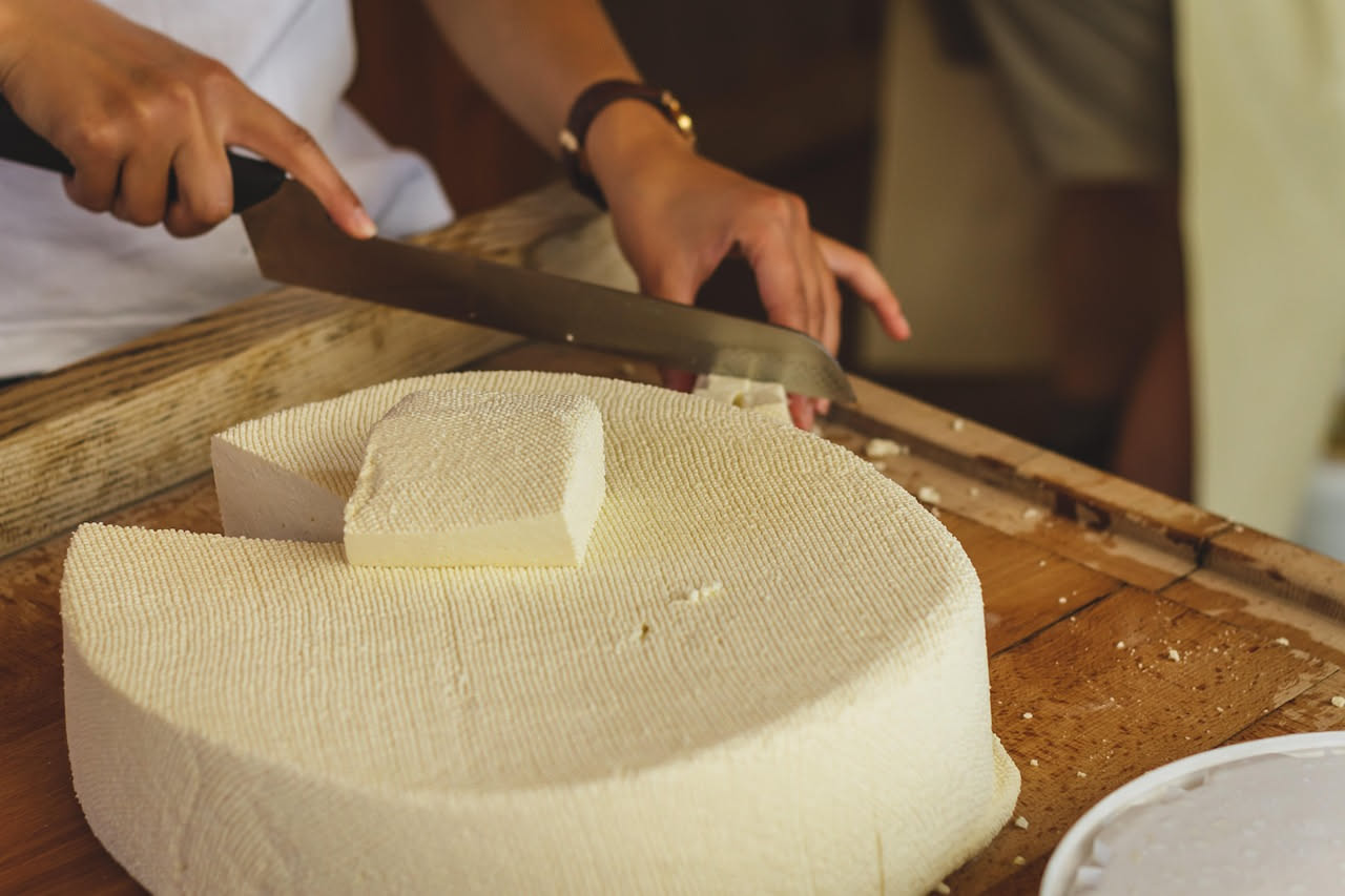 Crescenza fresca bianca e cremosa in una ciotola di vetro, con accanto un cucchiaio di legno e foglie di basilico fresco su tavolo di legno naturale