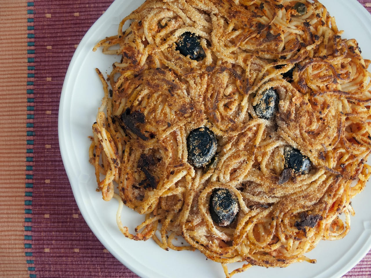 Tre crocchè di pasta dorati su un piatto bianco, uno tagliato a metà per mostrare l'interno cremoso con pezzi di pasta visibili, contorno di pomodorini rossi