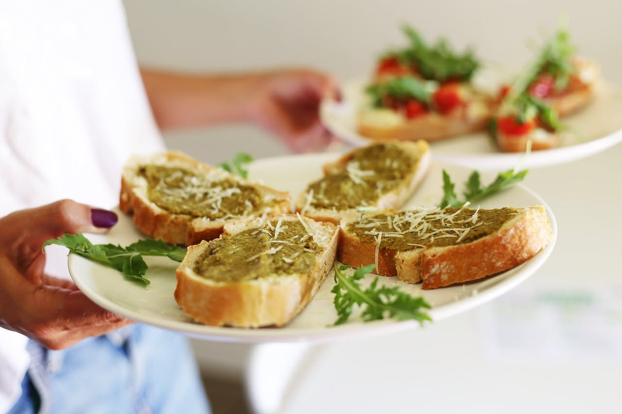 Quattro crostini tostati al burro con crema di fegatini color marrone scuro e rosmarino fresco, disposti su un tagliere di legno