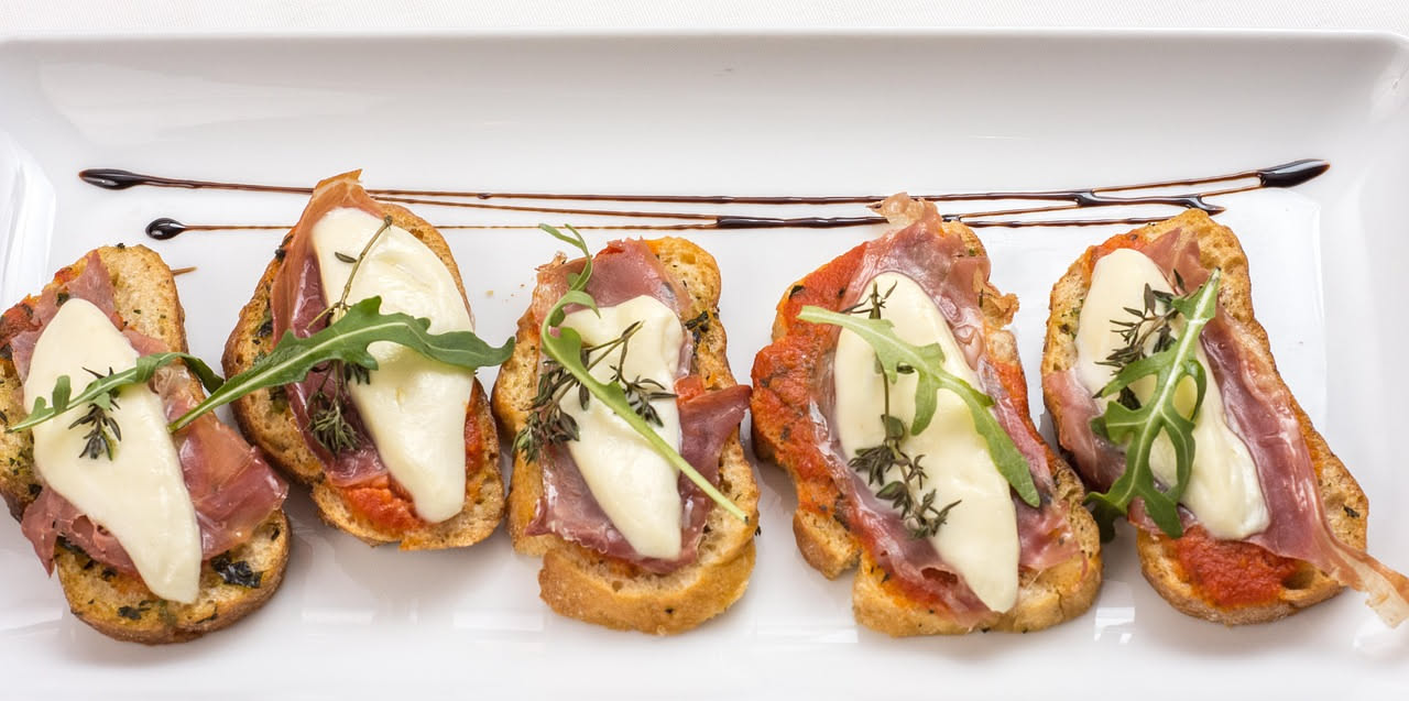 Crostini di pane tostato dorato su un piatto bianco, ricoperti di paté di fegatini color marrone scuro, con acciughe e capperi visibili in superficie