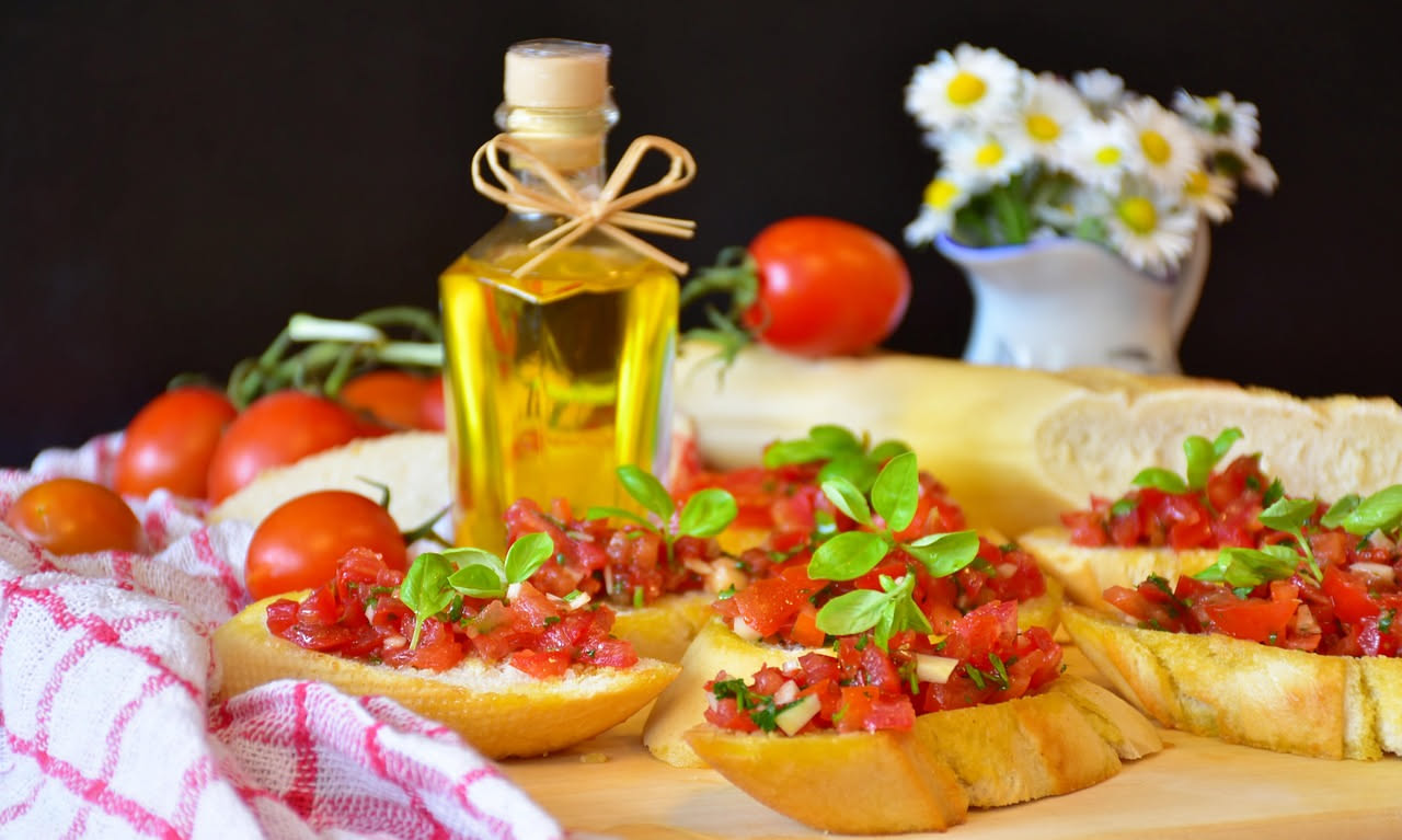 Crostini dorati disposti su un piatto bianco, ricoperti di ciccioli marroni croccanti, cosparsi di pepe nero, con uno spicchio d'aglio accanto e un canovaccio di lino sullo sfondo