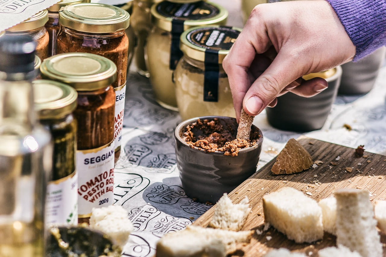 Crostini di fegatini di pollo su un piatto bianco: pane tostato ricoperto di pasta di fegatini marrone scuro, con visibili pezzi di alice e capperi verdi, accompagnati da un bicchiere di vino rosso