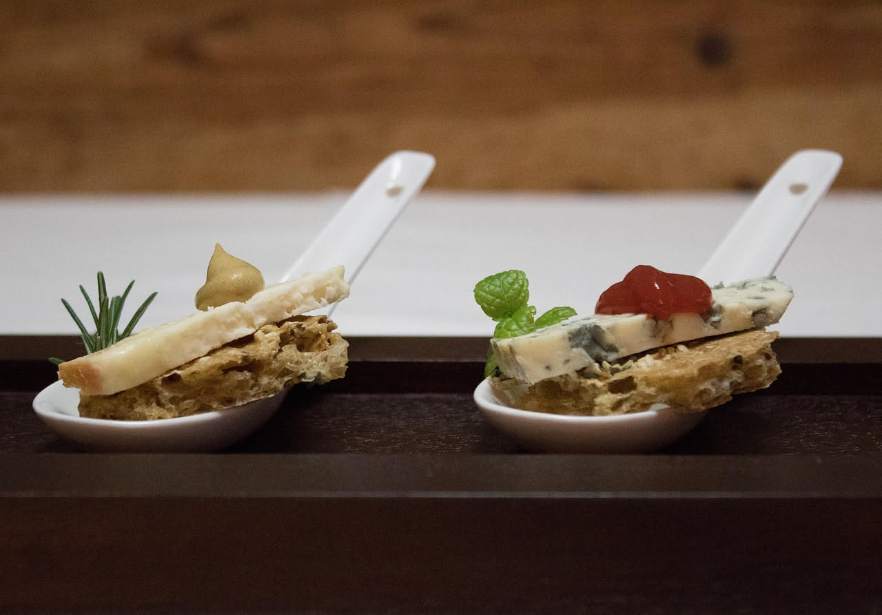 Crostini dorati con ricotta bianca cremosa, granelli di noci tostate e un filo di miele, disposti su una tavola di legno scuro con un bicchiere di vino bianco