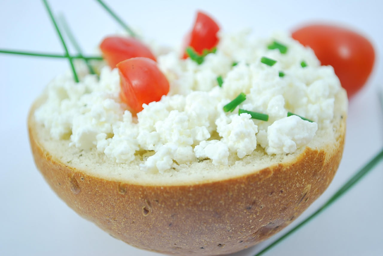 Crostini di ricotta su un piatto bianco, pane tostato leggermente dorato coperto di ricotta bianca cremosa, decorati con un filo d'olio e erbe aromatiche fresche