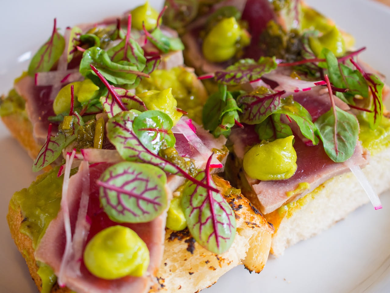Crostini di tonno disposti su un piatto bianco, con tonno cremoso spalmato sul pane dorato, decorati con un filo di olio d'oliva e una foglia di prezzemolo