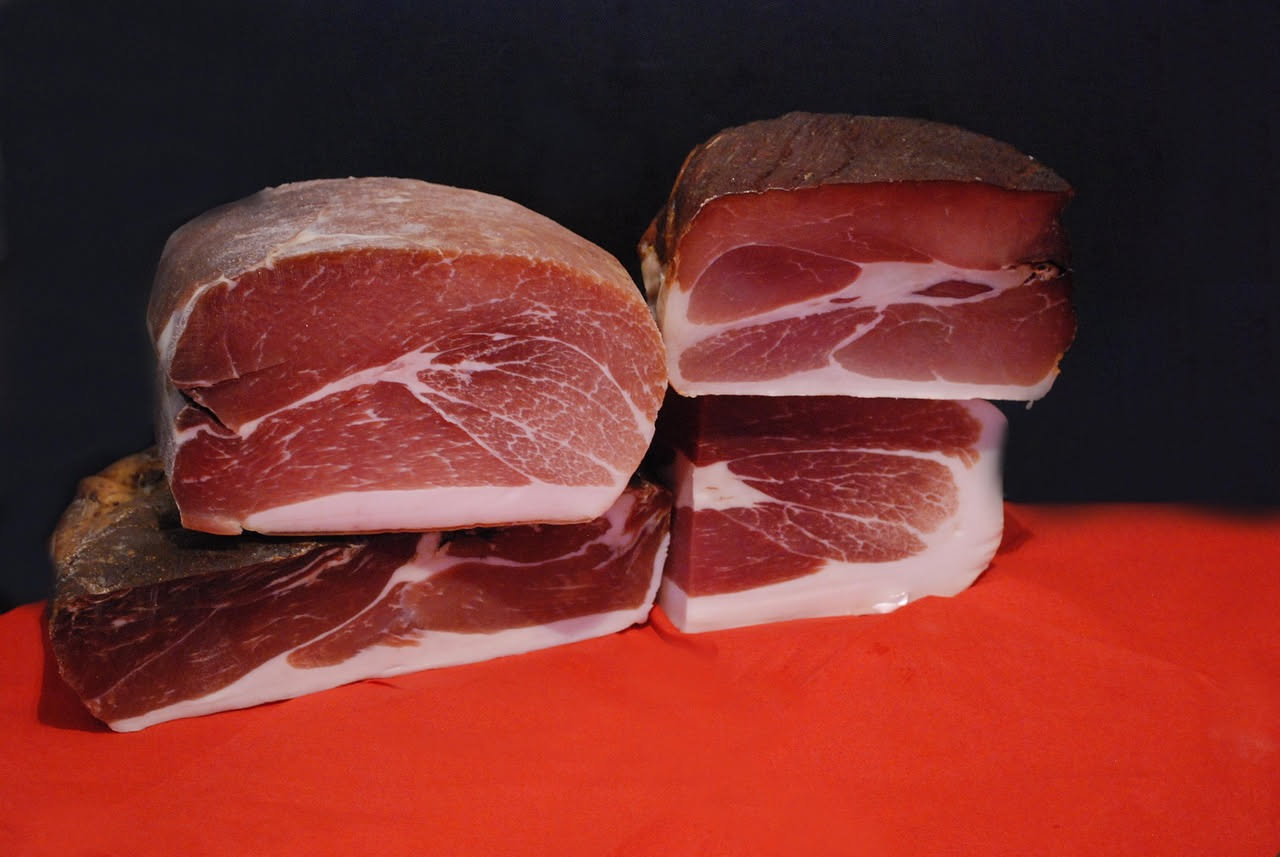 Culatello di Zibello affettato al coltello su un tagliere di legno, fette sottili e trasparenti, colore rosa antico, accanto a pane toscano e bicchiere di vino rosso