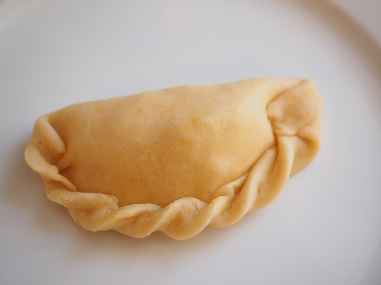 Culurgiones d'oru disposti su un piatto bianco, ricoperti di miele ambrato e mandorle tostate, colore dorato brillante, taglio netto che mostra il ripieno beige e scuro