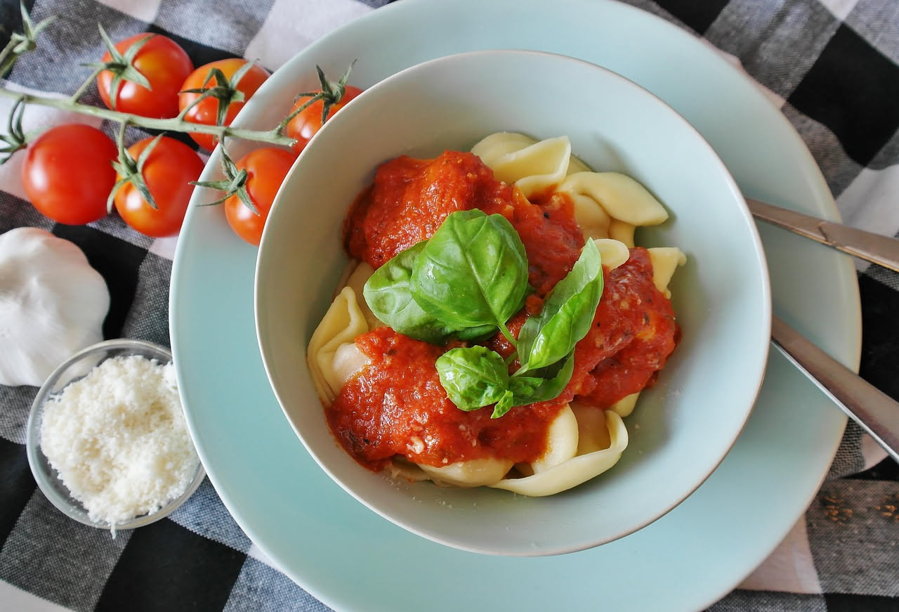 Culurgiones sardi disposti nel piatto, pasta dorata con caratteristica piega a intreccio, conditi con salsa di pomodoro leggera e pecorino romano grattugiato, due o tre pezzi in primo piano morbidi al