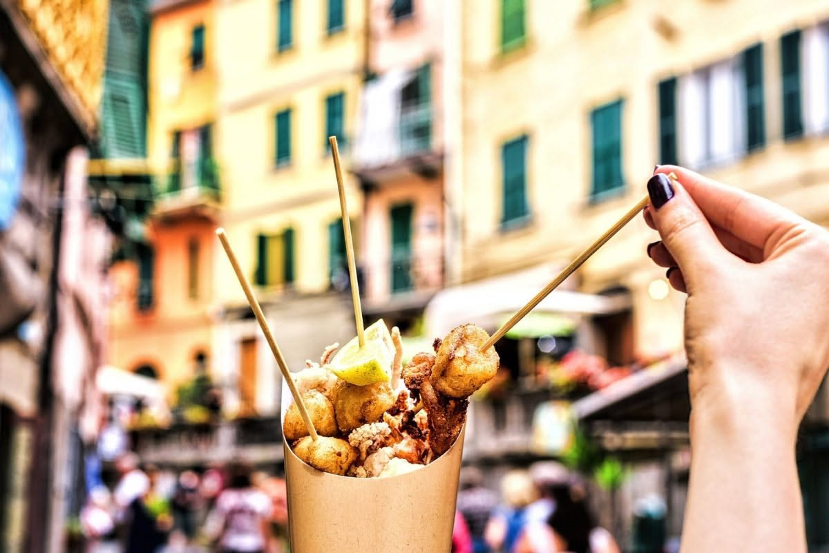 Un cartoccio di carta bianca pieno di verdure fritte dorate e croccanti, melanzane e zucchine tagliate a strisce, patate, con sale grosso sparso sopra