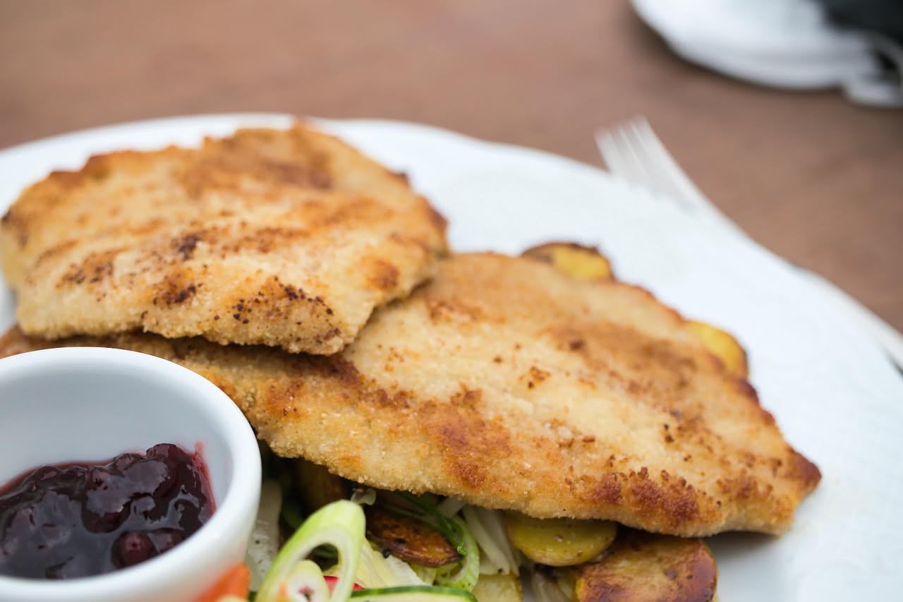 Cotoletta alla parmigiana dorata e croccante in piatto bianco, coperta di mozzarella filante e pomodoro rosso, bordo di parmigiano grattugiato, guarnizione di basilico fresco verde