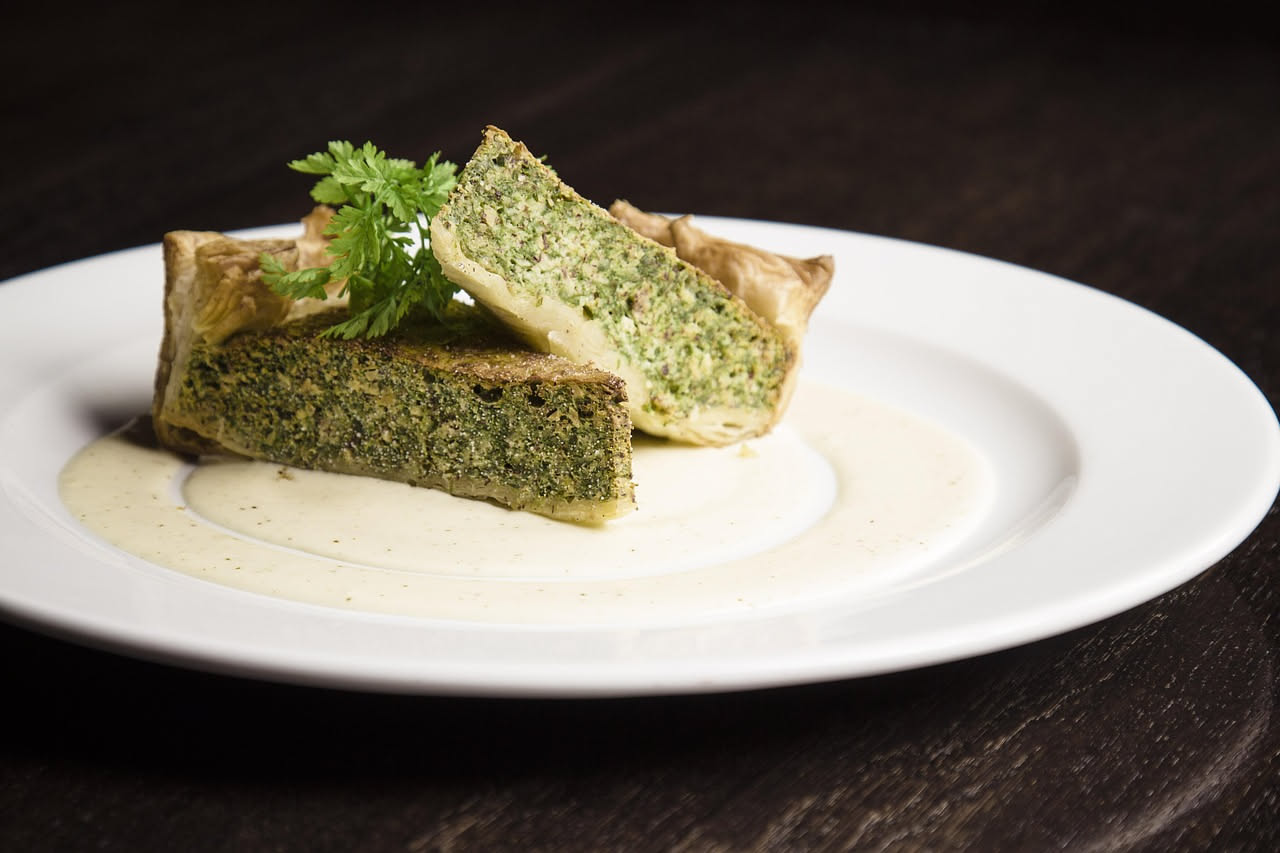 Erbazzone appena sfornato, tagliato in fette, con ripieno verde di verdure e formaggio filante, posato su un tavolo bianco con un coltello affilato accanto
