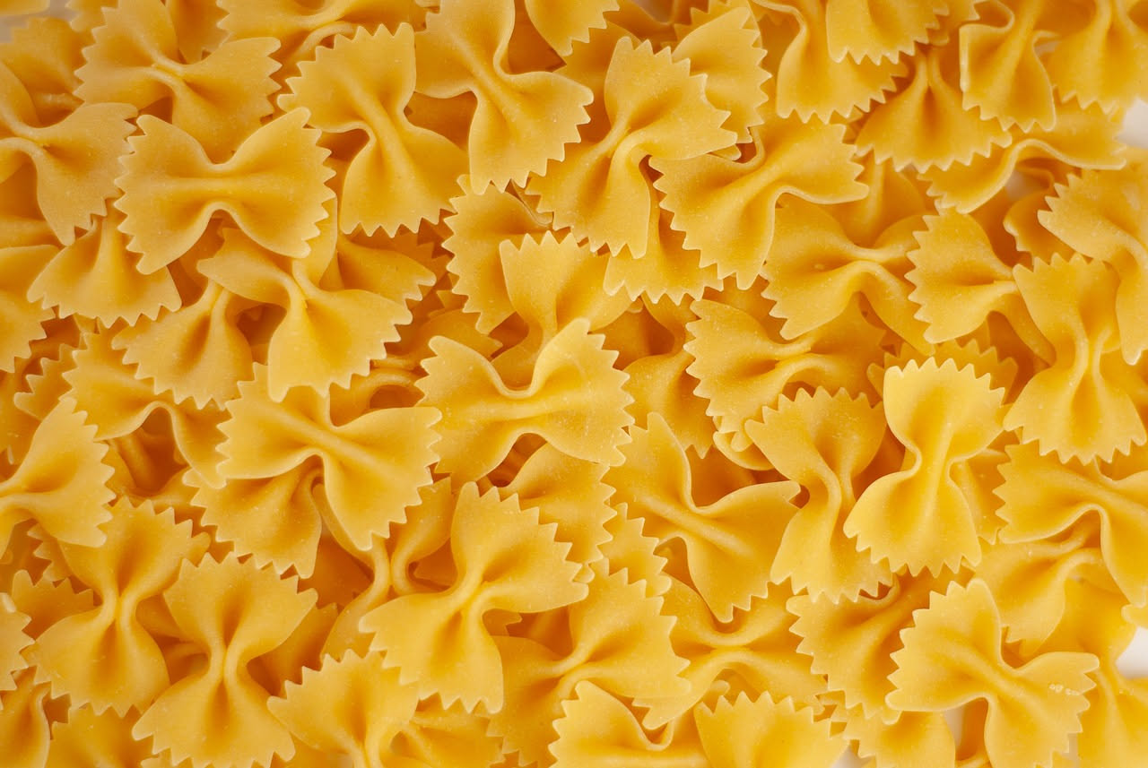Piatto fondo con farfalle al ragù di maiale, sugo rosso scuro che copre la pasta, grattugia di Parmigiano-Reggiano fresco, basilico verde appena colto, sfondo bianco in ceramica satinata