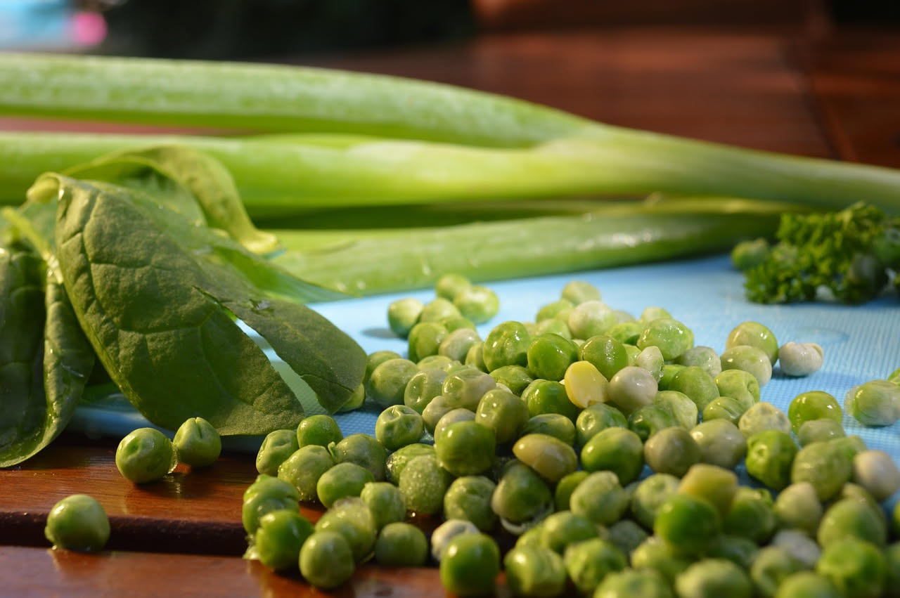 Piatto bianco con fave giallo-verdi leggermente schiacciate al centro, coperte da cicoria lessa verde scuro, con un filo di olio d'oliva dorato in superficie e una spruzzata di pepe nero