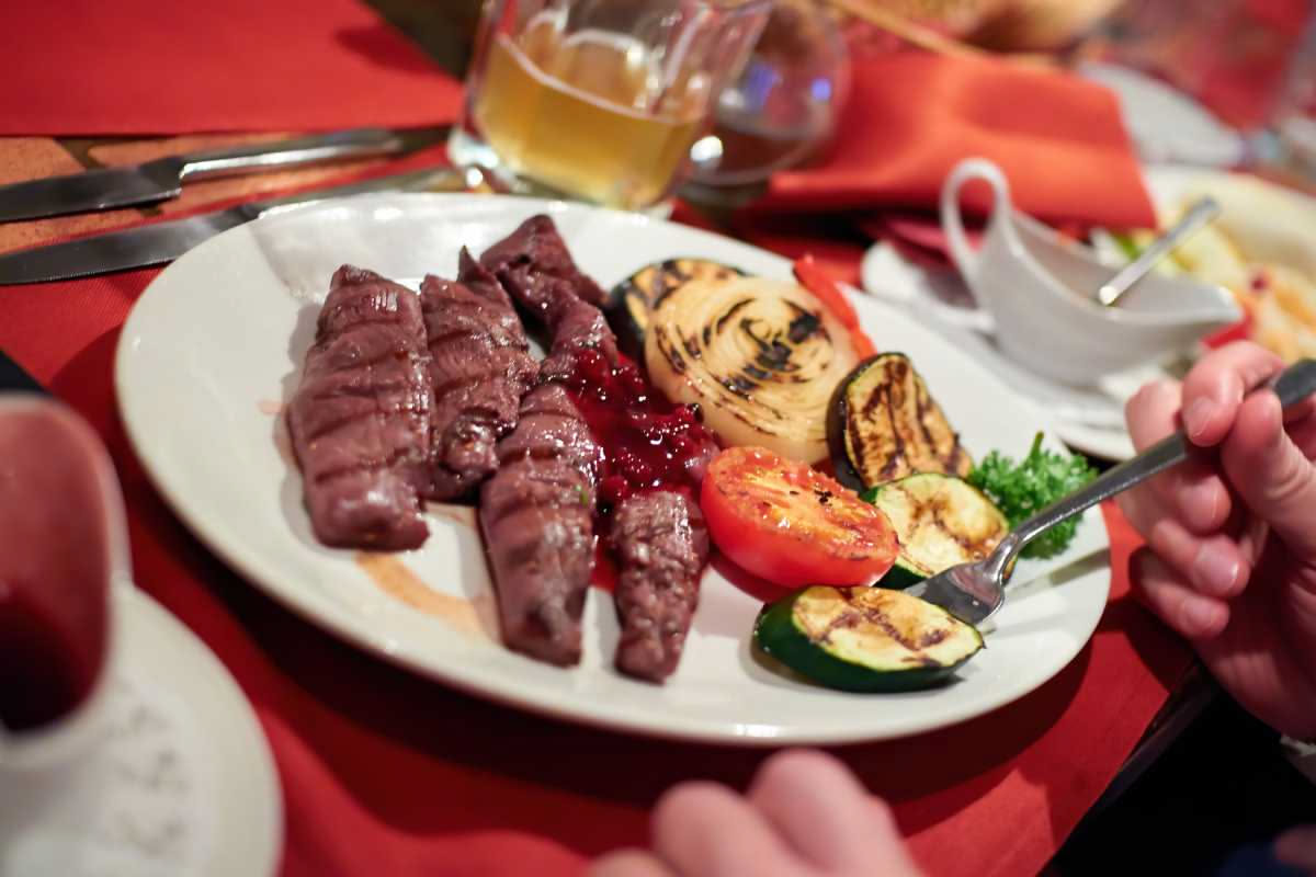 Piatto di fegato di maiale in umido con salsa rossa, cipolla caramellata e prezzemolo fresco, su fondo scuro di tavolo in legno