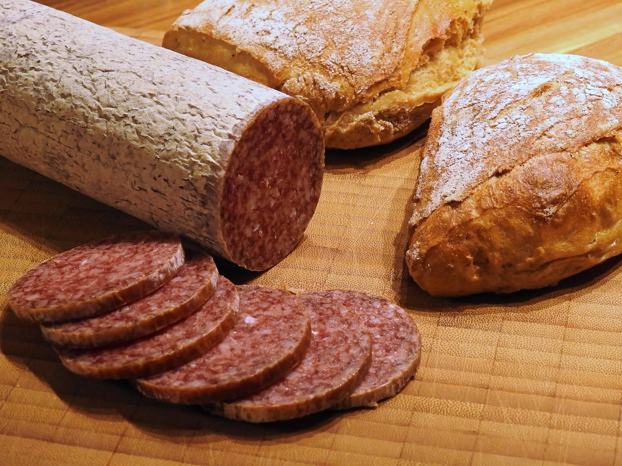 Fette di finocchiona rosa e bianca su un tagliere di legno, con i semi di finocchio visibili sulla superficie, con un coltello accanto