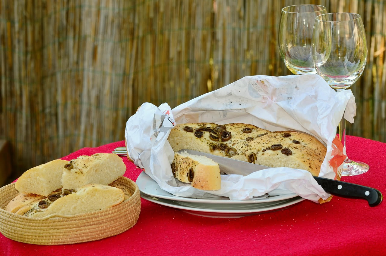 Focaccia d'Oneglia intera su una tavola di legno, dorata e oleosa, con cristalli di sale grosso visibili sulla superficie, tagliata in quattro quadrati