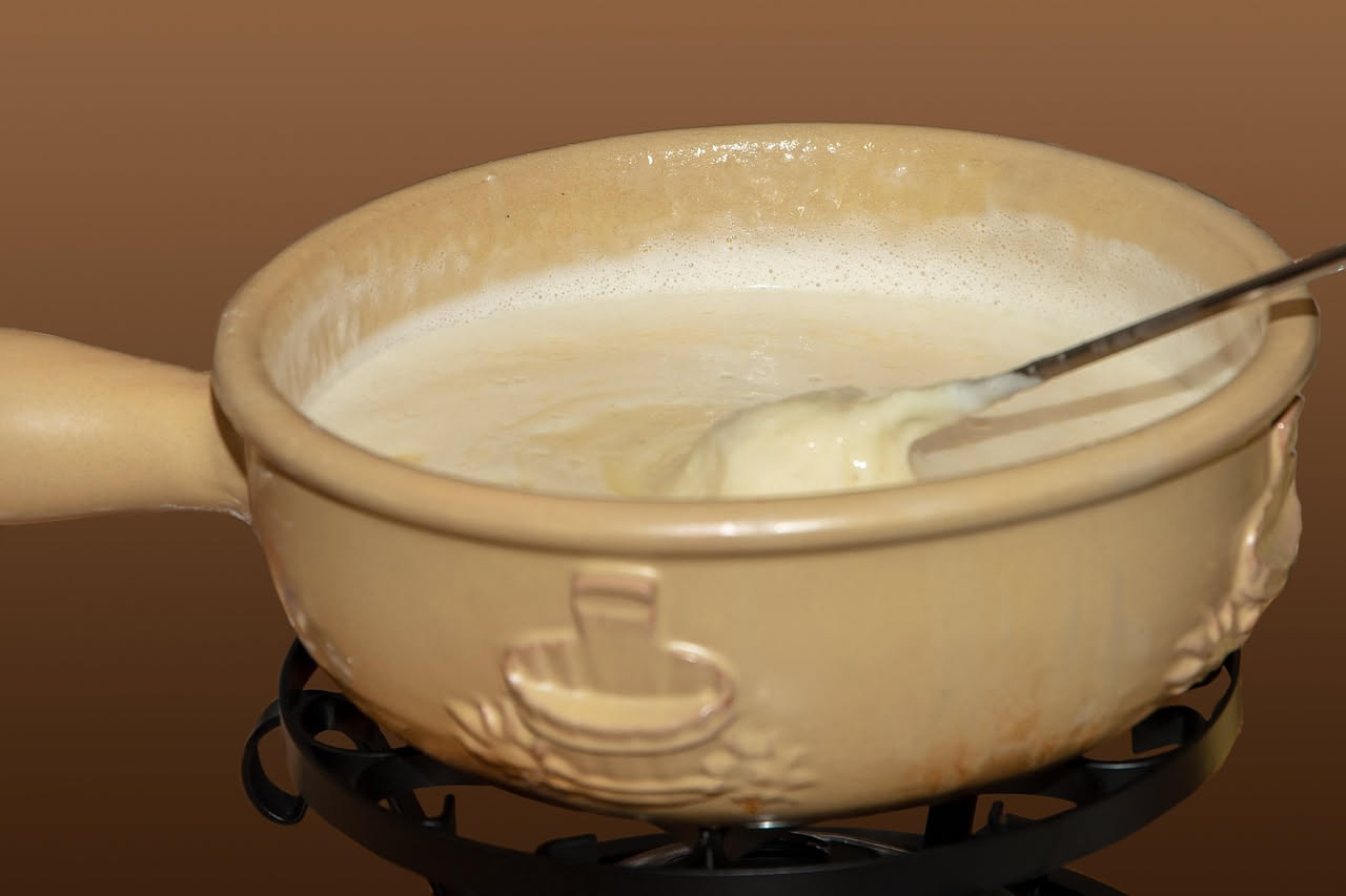 Fonduta cremosa giallo dorato servita in caquelon di ceramica, con due forchette a lungo stelo immerse nel formaggio fuso, pane tostato e verdure crude nel piatto intorno