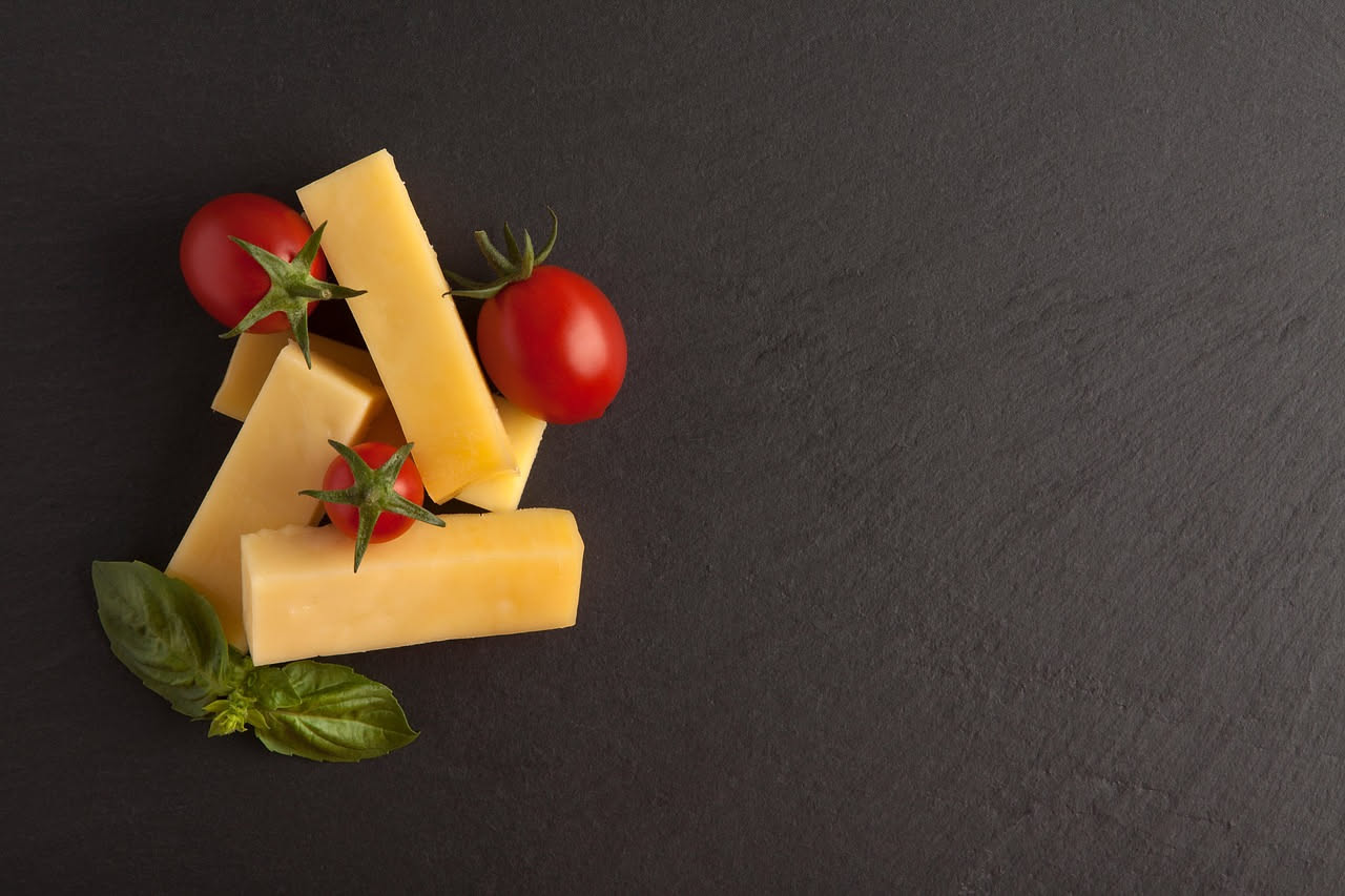 Quattro blocchi di formaggi affumicati di diversi colori dal giallo pallido al marrone scuro, disposti su un tavolo di legno rustico con un coltello da formaggio e un piatto bianco sullo sfondo