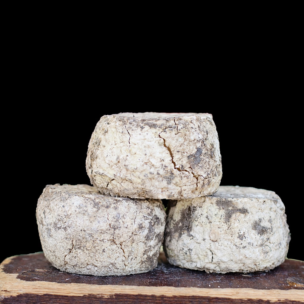 Due forme di formaggio d'alpeggio a pasta semidura, di colore giallo paglierino, con crosta naturale rugosa, tagliate a spicchi. In sottofondo prato di montagna con fiori alpini e pastore con gregge a