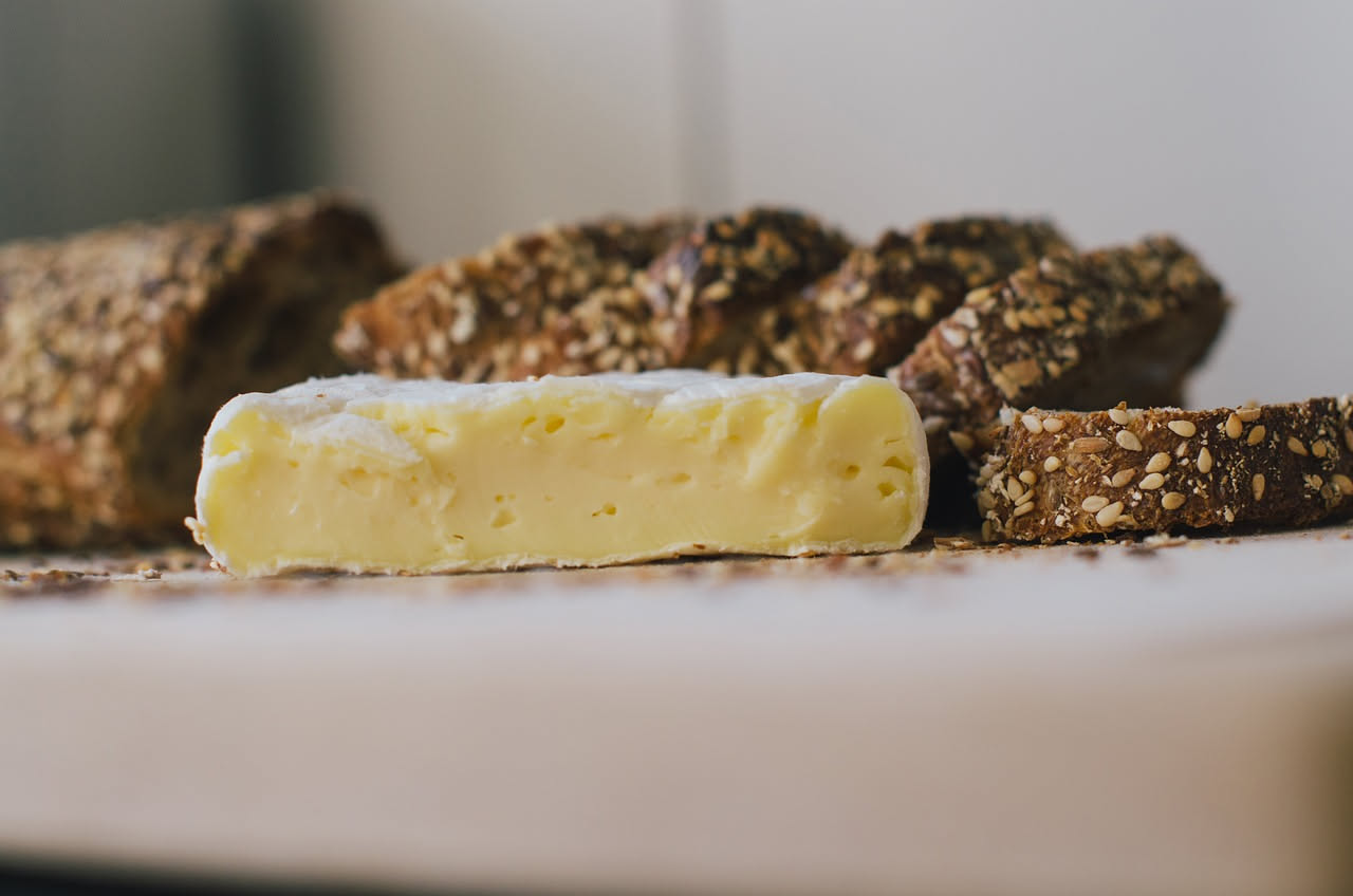 Formaggio di fossa tagliato a fette su un tagliere di legno, colore giallo paglierino con screziature scure, accompagnato da miele e noci, su fondo rustico naturale