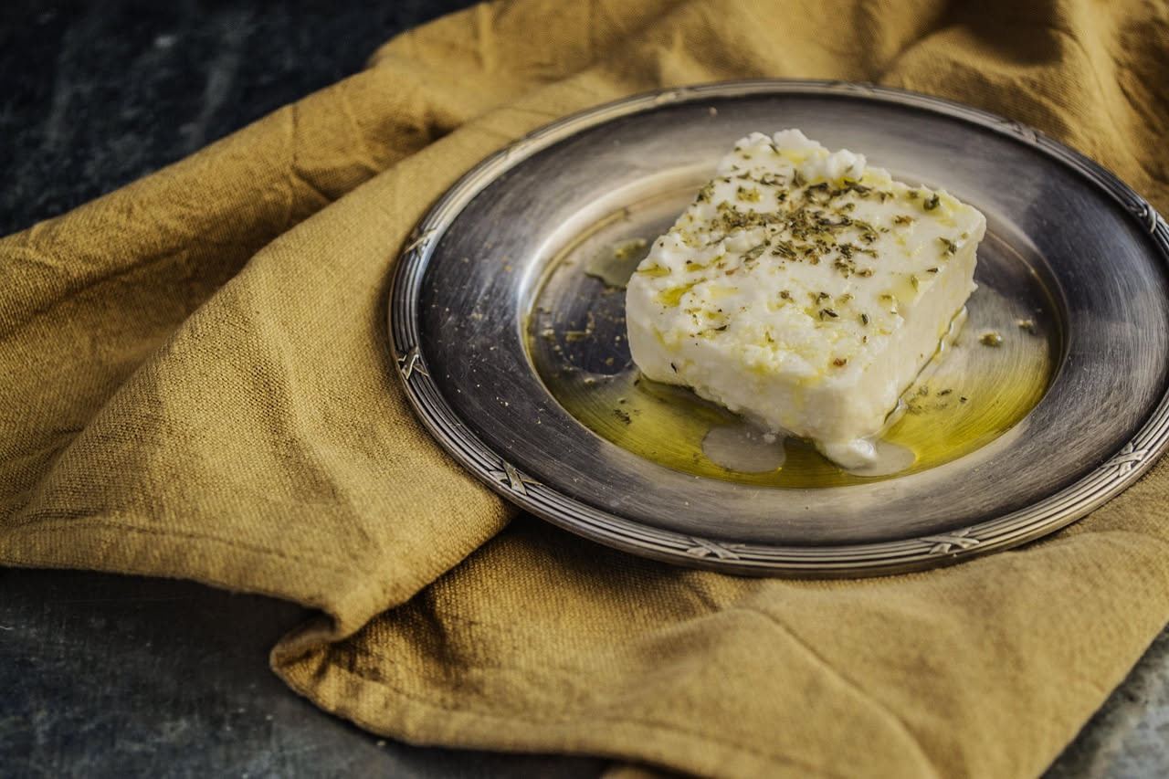 Formaggio fresco bianco cremoso servito in una ciotola di ceramica con un cucchiaio di legno, contorno di pane tostato e miele liquido versato sopra