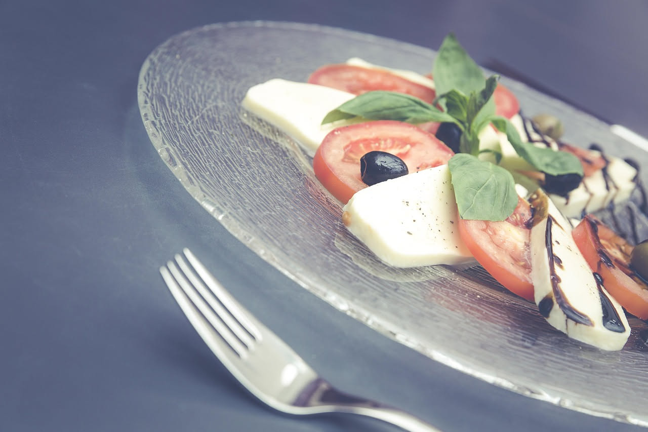 Formaggio vaccino fresco bianco cremoso appena tolto dalla garza, servito in una ciotola di ceramica con gocce di miele scuro e fragole rosse tagliate a metà, sfondo di legno chiaro