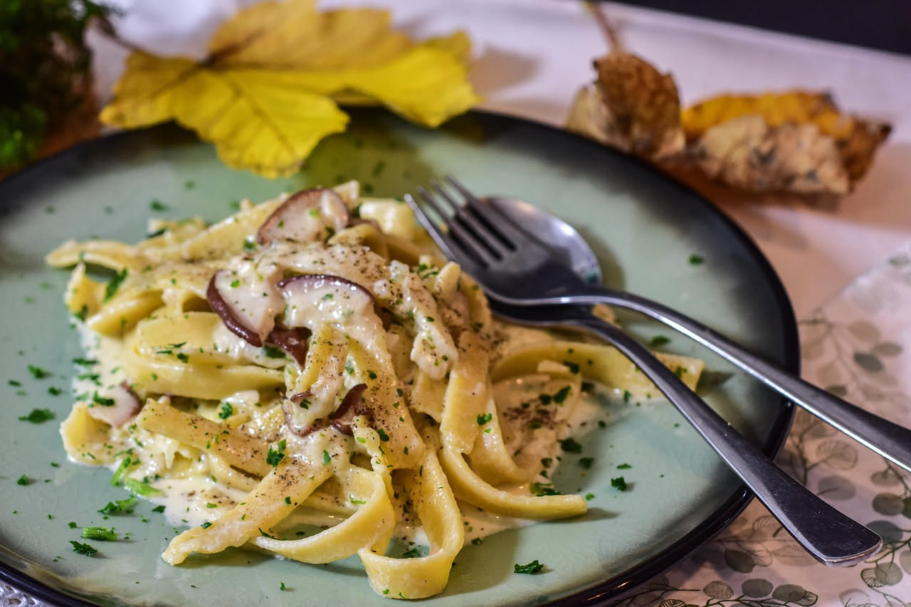 Piatto di frascatelli dorati con funghi trifolati, prezzemolo fresco verde e un filo di olio extravergine, serviti in una ciotola di ceramica bianca