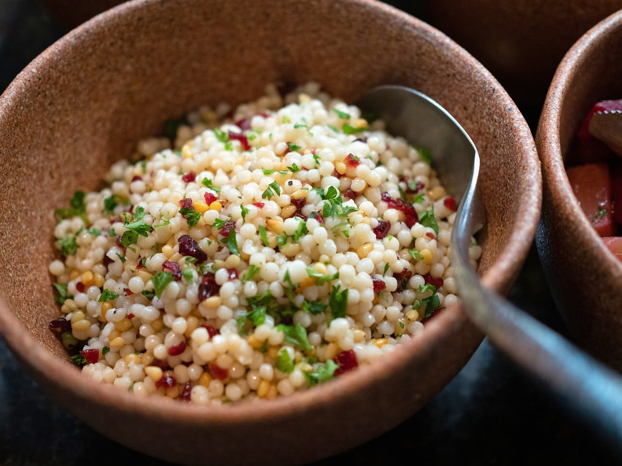 Un piatto di fregola bianca e granulosa condita con scaglie dorate di botarga, gocce di olio d'oliva lucente, pepe nero e prezzemolo fresco su sfondo chiaro