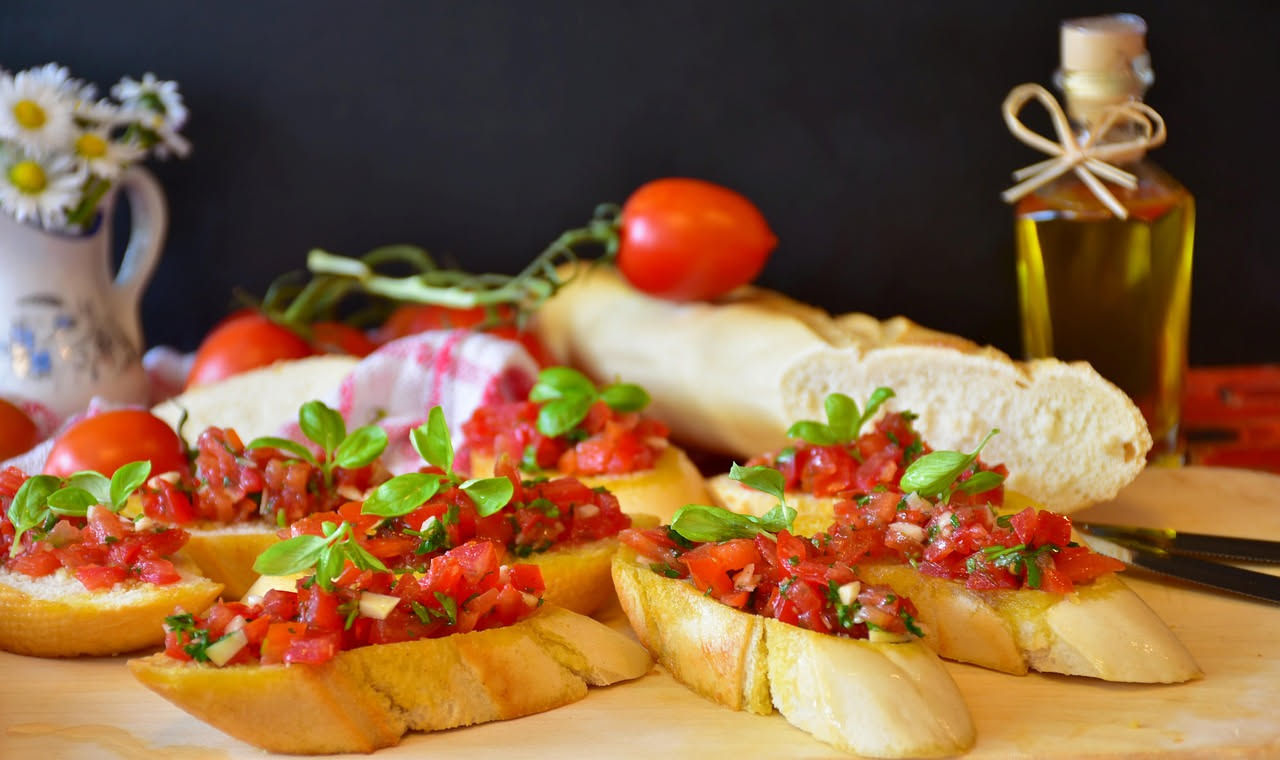 Tre friselle dorate e croccanti appoggiate su un piatto bianco, tagliate a metà, riempite visibilmente di pomodoro rosso fresco e cipolla bianca, con un filo d'olio lucido in superficie e una manciata