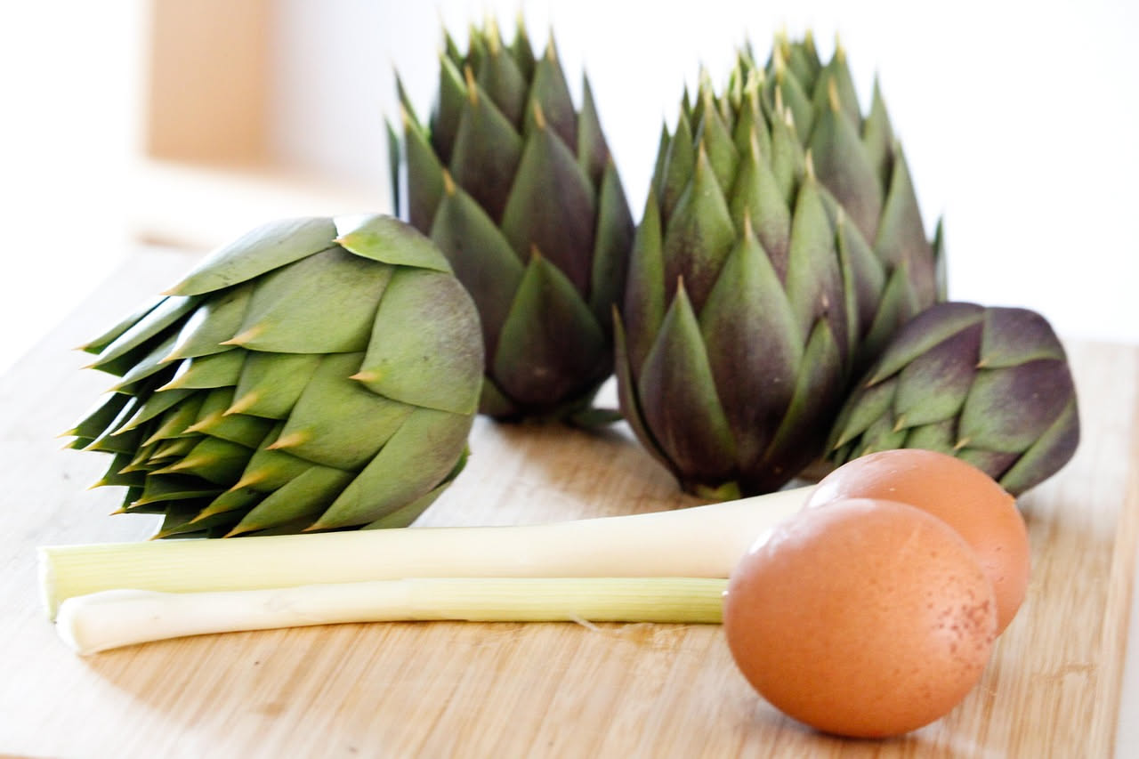 Frittata di carciofi dorata in padella antiaderente, ripiena di fette di carciofi teneri e bordi leggermente croccanti, con uova dorate visibili in trasparenza