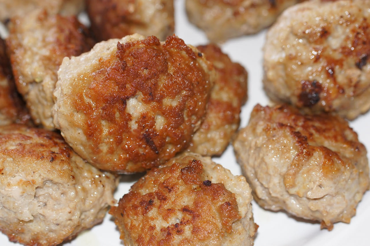 Frittelle di carne disposte su un piatto bianco, dorate e croccanti, guarnite con prezzemolo fresco. Sfondo neutro con una forchetta a lato.